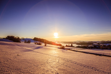 Fototapeta na wymiar Sunset scenery in Winter: Lake, snowy fields and sundown. Wallersee, Austria