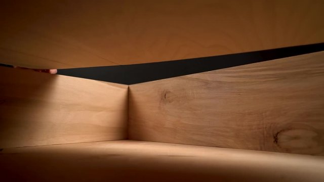 A view from inside of a man's hand opening a wooden box and touching its walls. A carpenter is removing a plywood board to open the drawer