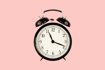 Black retro alarm clock on pink background closeup