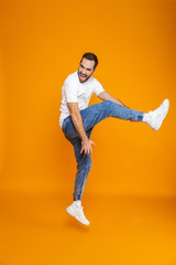Fototapeta na wymiar Full length photo of optimistic guy in t-shirt and jeans jumping and having fun, isolated over yellow background