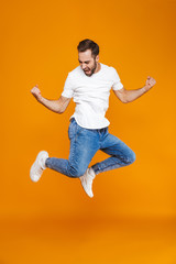 Fototapeta na wymiar Full length photo of smiling guy in t-shirt and jeans jumping and having fun, isolated over yellow background