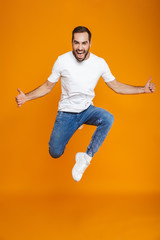 Fototapeta na wymiar Full length photo of cheerful guy in t-shirt and jeans jumping and having fun, isolated over yellow background