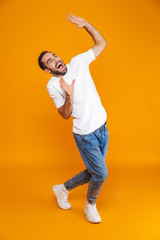 Fototapeta na wymiar Full length image of cheerful guy 30s in t-shirt and jeans raising hands while standing, isolated over yellow background