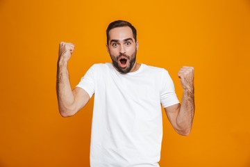 Fototapeta premium Image of brunette man 30s with beard and mustache clenching fists in joy while standing, isolated over yellow background