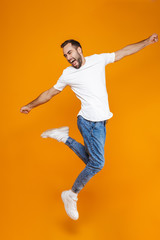 Fototapeta na wymiar Full length photo of attractive guy in t-shirt and jeans jumping and having fun, isolated over yellow background