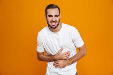 Image of caucasian man 30s in t-shirt bending and touching his belly because of pain while,...