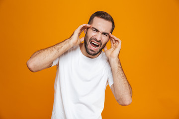 Fototapeta premium Image of sick guy 30s in t-shirt screaming and rubbing temples because of headache while, isolated over yellow background