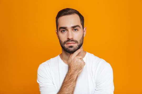 Image of caucasian man 30s in t-shirt touching his chin while standing, isolated over yellow background