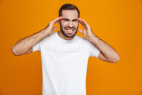 Image of young guy 30s in t-shirt screaming and rubbing temples because of headache while, isolated over yellow background