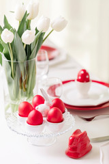 Obraz na płótnie Canvas Happy easter. Decor and table setting of the Easter table is a vase with white tulips and dishes of red and white color. Easter colored eggs with white polka dots.