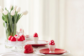 Happy easter. Decor and table setting of the Easter table is a vase with white tulips and dishes of red and white color. Easter colored eggs with white polka dots.