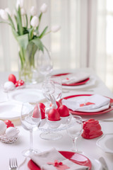 Happy easter. Decor and table setting of the Easter table is a vase with white tulips and dishes of red and white color. Easter colored eggs with white polka dots.