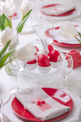 Happy easter. Decor and table setting of the Easter table is a vase with white tulips and dishes of red and white color. Easter colored eggs with white polka dots.