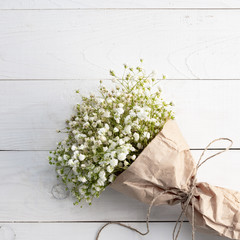 Beautiful bouquet in Kraft paper on wooden white background, copy space.