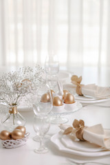 Happy Easter! Golden decor and table setting of the Easter table with white dishes of white color.