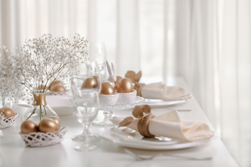 Happy Easter! Golden decor and table setting of the Easter table with white dishes of white color.