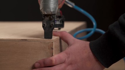 A bottom up shot of a man's hand holding pneumatic staple gun and stapling a plywood board to wooden box