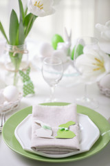 Decor and table setting of the Easter table with white tulips and dishes of green and white color. Easter decor in the form of Easter bunnies  green color with white polka dots.