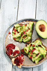 sliced avocado and ripe pomegranates on toast bread with spices and avocado.