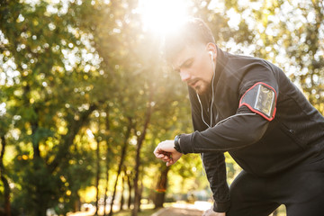 Naklejka na ściany i meble Handsome young sports fitness man runner outdoors in park listening music with earphones.
