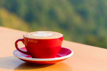 Morning hot latte art coffee in a red cup on wooden balcony at the hillside.