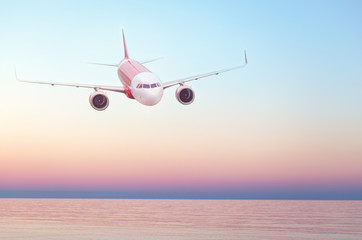 Fototapeta na wymiar Plane flying in the sky, summer travel flight, airplane over water, flight over skyline. Sunset over the sea. Empty place for text, copy space..
