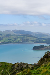 Tiny boat cussing trough blue bay surrounded by green mountains on sunny day with dramatic sky