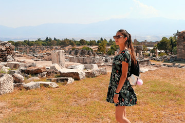 girl in a dress with a briefcase looks away against the background of the ancient city, ruins, summer