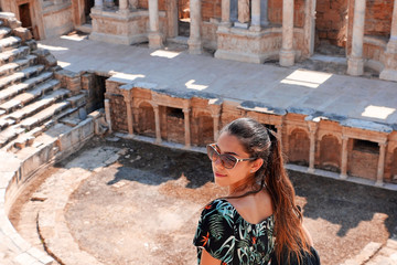 girl in a dress with a briefcase looks away against the background of the ancient city, ruins, summer