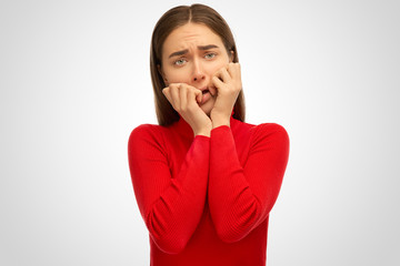 A frightened young girl frowns and covers her face with her hands. The concept of frustration of fear and surprise. Studio portrait on isolated white background