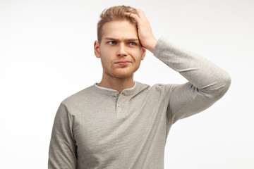 Attractive trendy young male freelancer with beard looking away with confused disappointed expression, scratching head. Handsome guy student remembers information for exam.