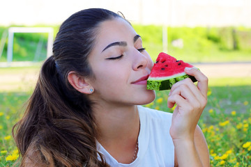 portrait of a girl with dark hair holds a juicy watermelon and enjoys, on a background of green field
