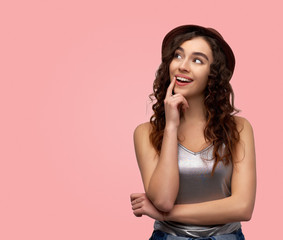 Indoor shot of happy young woman keeps hand under chin, looks joyfully look away, has healthy skin, shows natural beauty, being in good mood, isolated over pink background