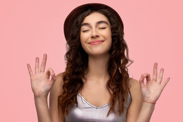 Cheerful brunette young female with glad expression, shows ok sign with both hands, dressed in...