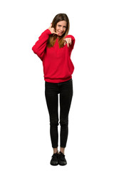 Fototapeta premium A full-length shot of a Young woman with red sweater making phone gesture and pointing front over isolated white background
