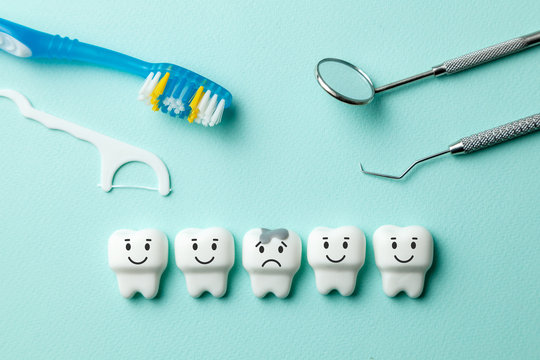 Healthy white teeth are smiling and tooth with caries is sad on green mint background. Toothbrush and dentist tools mirror, hook.