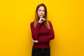 Woman with turtleneck over yellow wall showing a sign of silence gesture putting finger in mouth