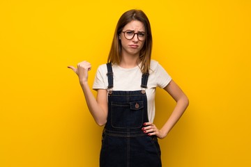 Woman over yellow wall unhappy and pointing to the side