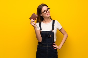 Woman over yellow wall holding a wallet - obrazy, fototapety, plakaty