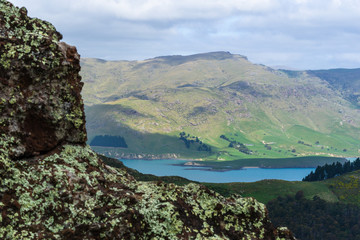 Rocks in foreground and bay surrounded by green mountains in the background