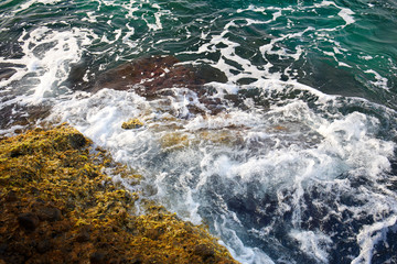 Aerial top view of sea waves hitting rocks on the beach with turquoise sea water. Amazing rock cliff seascape in the coastline. Aerial view of sea waves and fantastic Rocky coast. Mediterranean Sea.