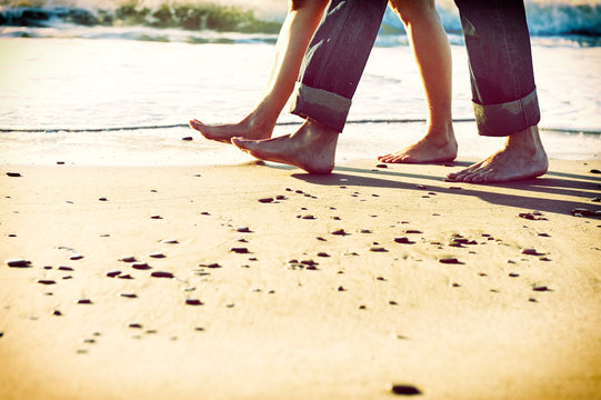 Pies descalzos de pareja paseando por la orilla de la playa al amanecer