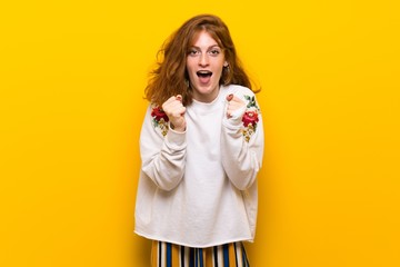 Young redhead woman over yellow wall celebrating a victory in winner position