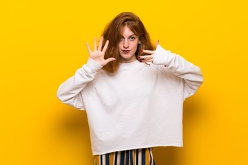 Young redhead woman over yellow wall counting nine with fingers