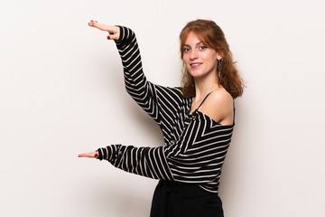 Young redhead woman over white wall holding copyspace to insert an ad