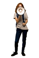 A full-length shot of a Young redhead student shouting through a megaphone over isolated white background