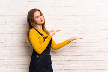 Teenager girl over white brick wall holding copyspace imaginary on the palm to insert an ad