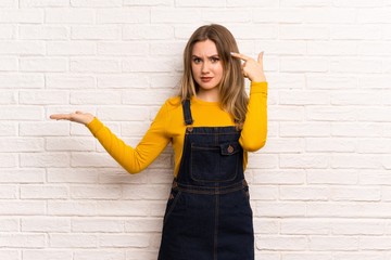 Teenager girl over white brick wall making the gesture of madness putting finger on the head