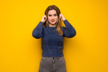 Teenager girl over yellow wall frustrated and covering ears with hands