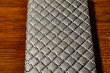 A book, a notebook with a checkered pattern on a wooden table in different poses. The cover is grey and soft with texture. Square patterns stitched with threads. Write notes in a diary. Plain white pa